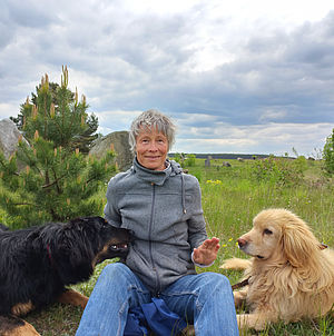 Die Zertifizierte Natur- und Landschaftsführerin Katrin Krause sitzt mit ihren beiden Hunden im Findlingspark Henzendorf.