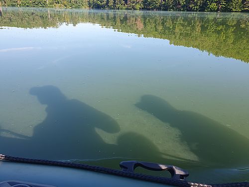 Zwei Ranger sitzen während der Komplexkontrolle auf einem Schlauchboot. Ihre schattigen Silhouetten sind auf der Wasseroberfläche zu sehen.